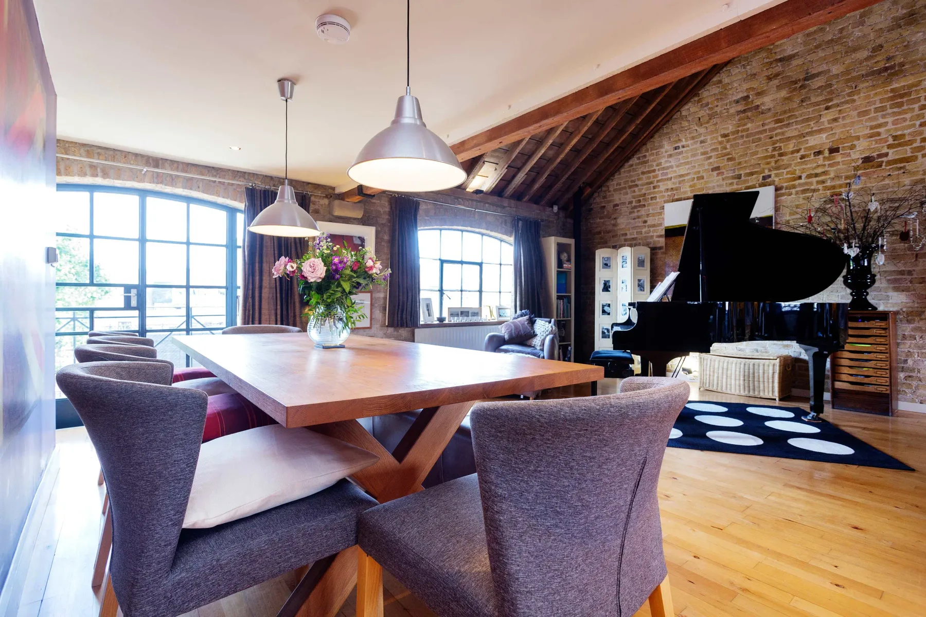 A bright loft living area with a dining table, seating, and a piano.