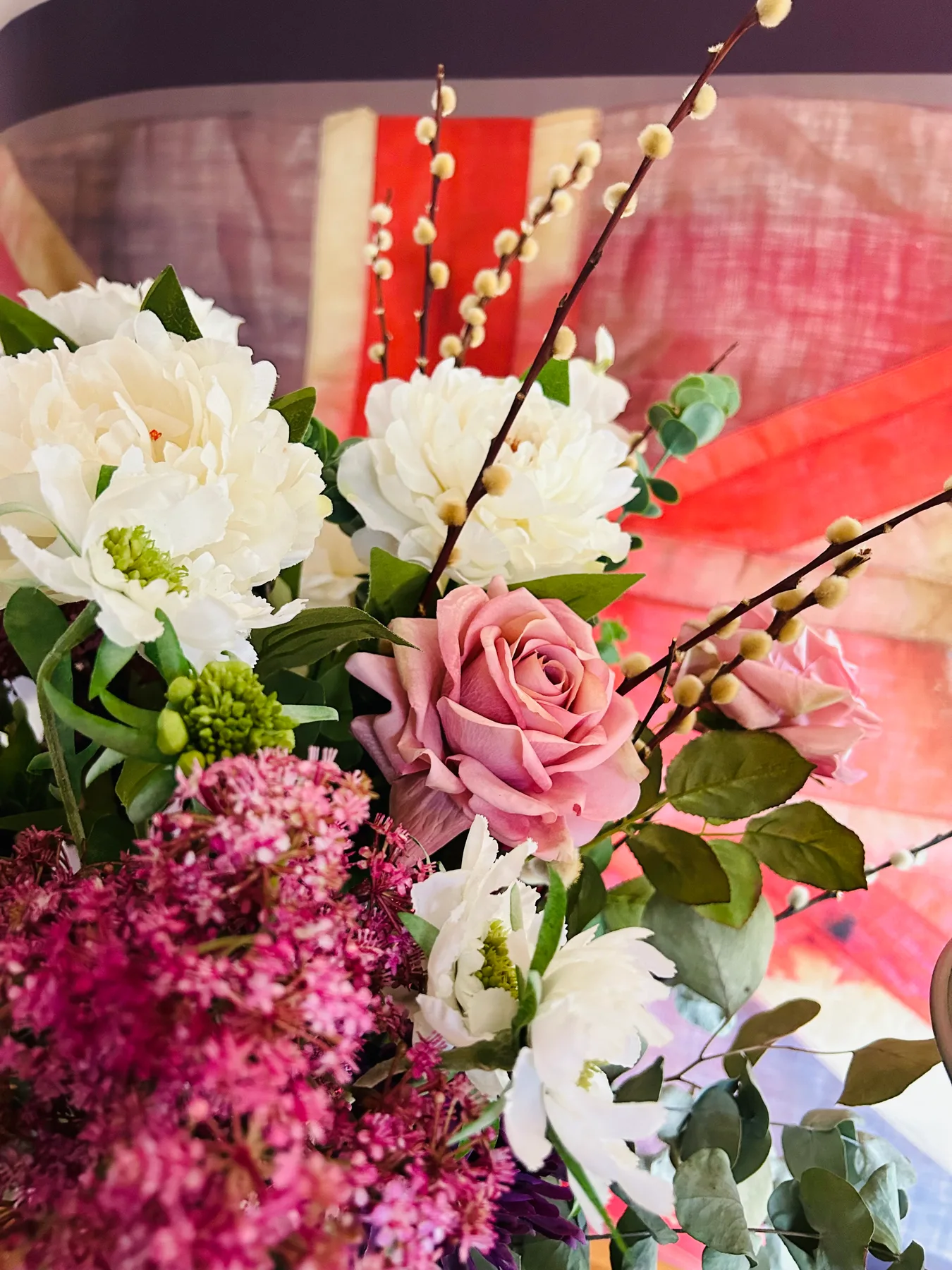 A colorful floral arrangement features a pink rose, white blooms, and leafy greenery.