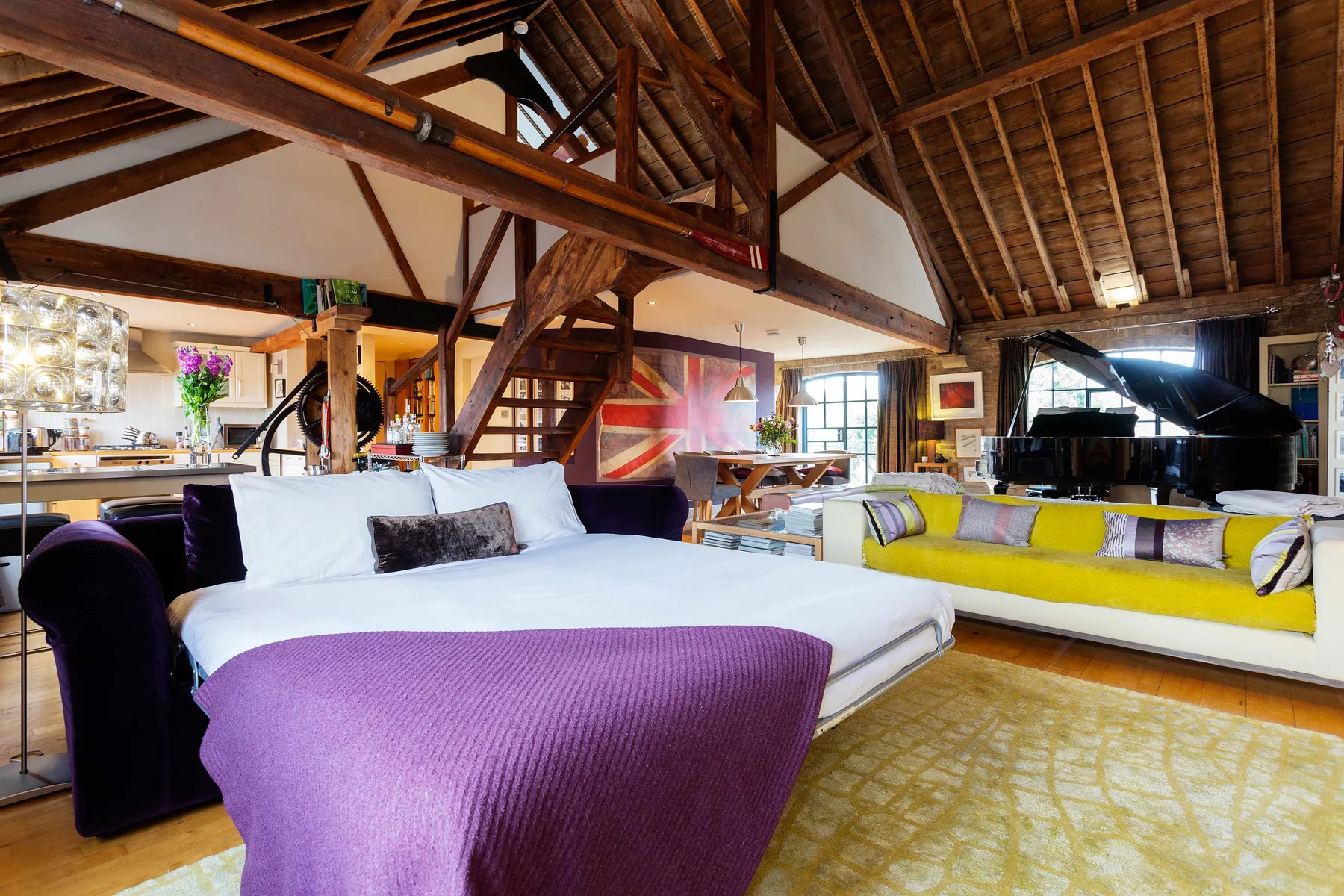 An open-plan living area with seating, a grand piano, and exposed timber beams.
