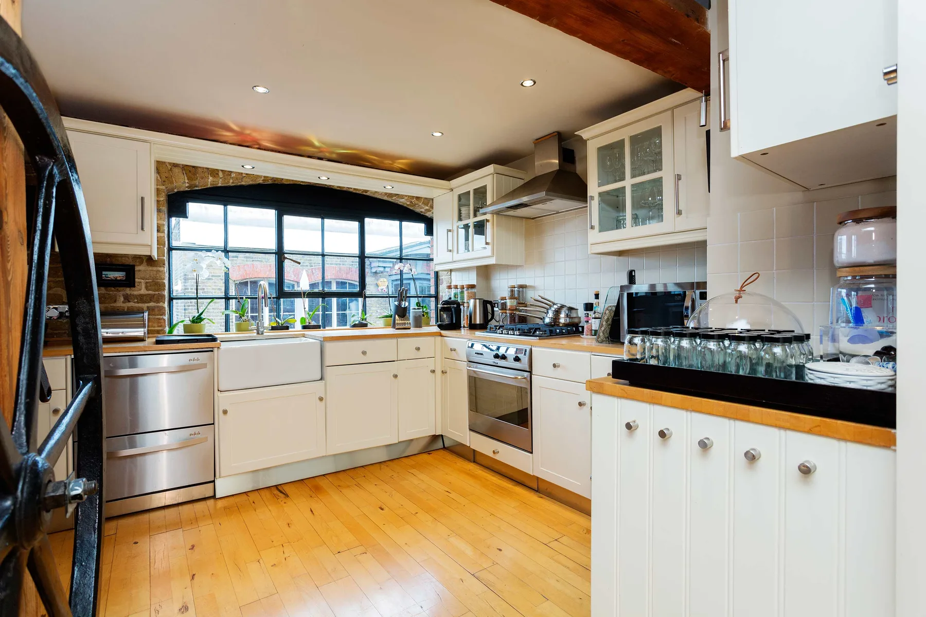 A bright kitchen with white cabinets, wood flooring, and a large window.