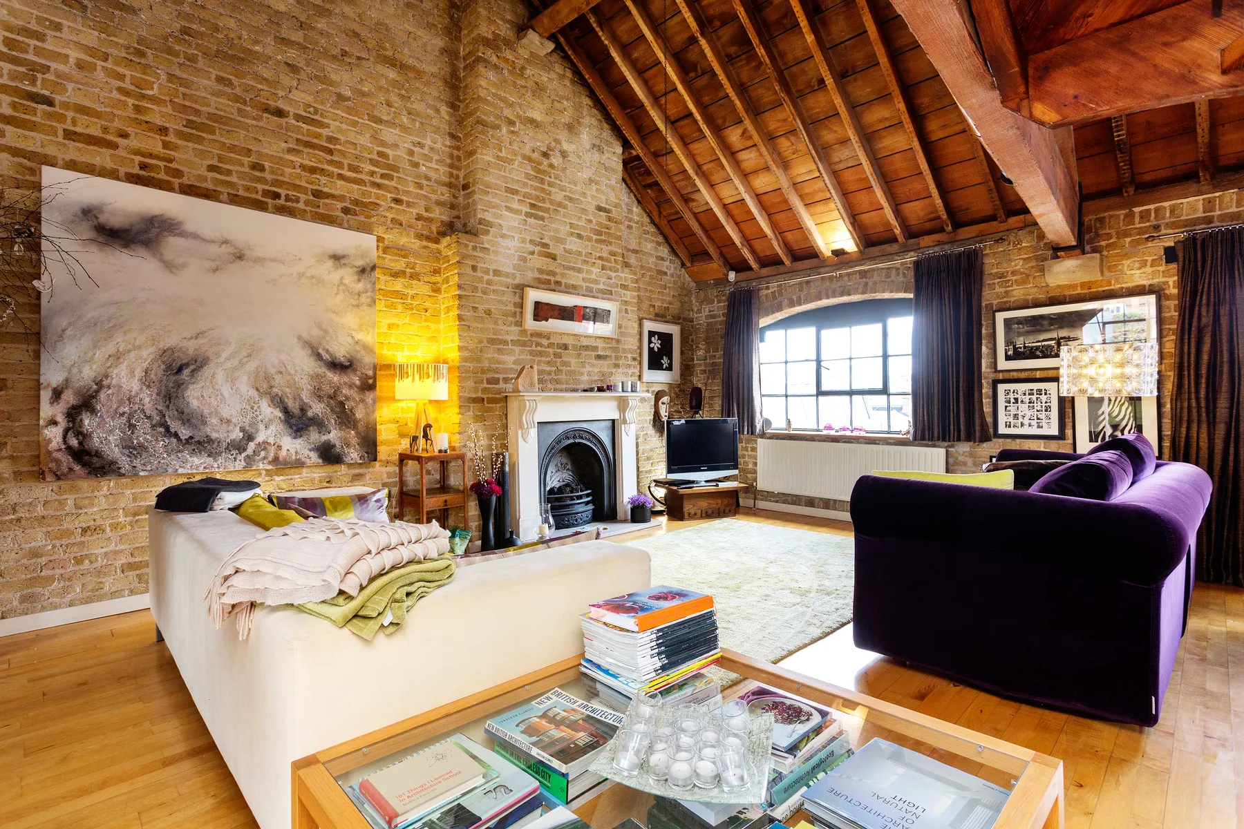 A spacious living room with exposed brick walls, a fireplace, and purple seating.