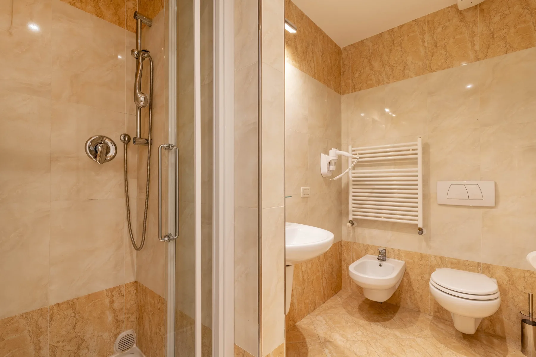 A tiled bathroom with a shower, sink, bidet, and toilet.