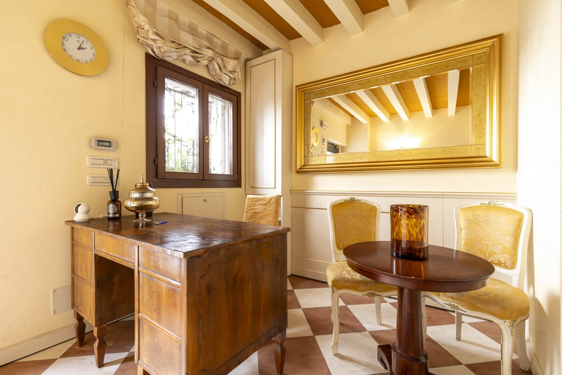 A dining area with a wooden table, two chairs, and a large wall mirror.