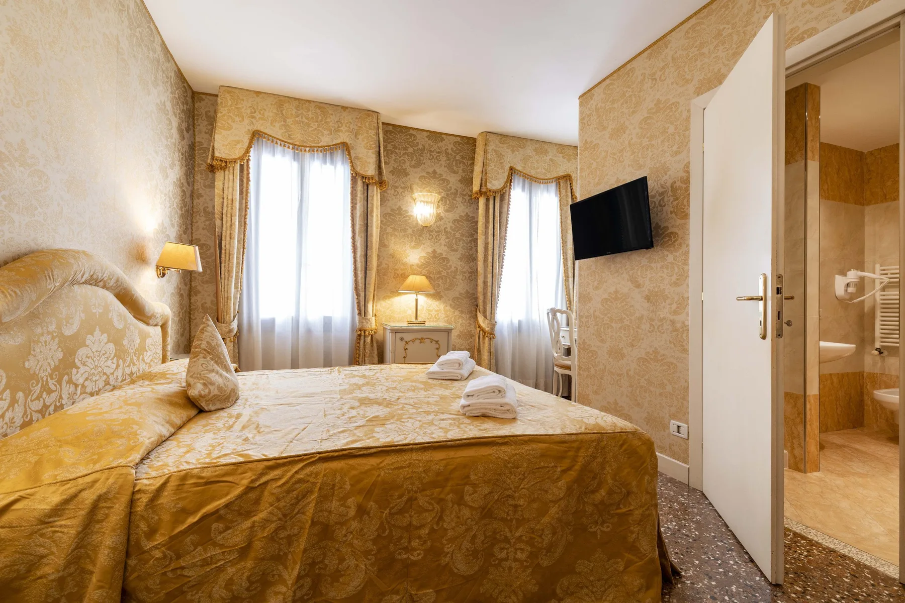A bedroom with a bed, tall windows, and an open doorway to the bathroom.