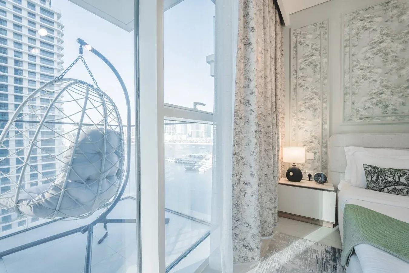Un dormitorio con una cama junto a una ventana amplia con vistas a edificios cercanos.