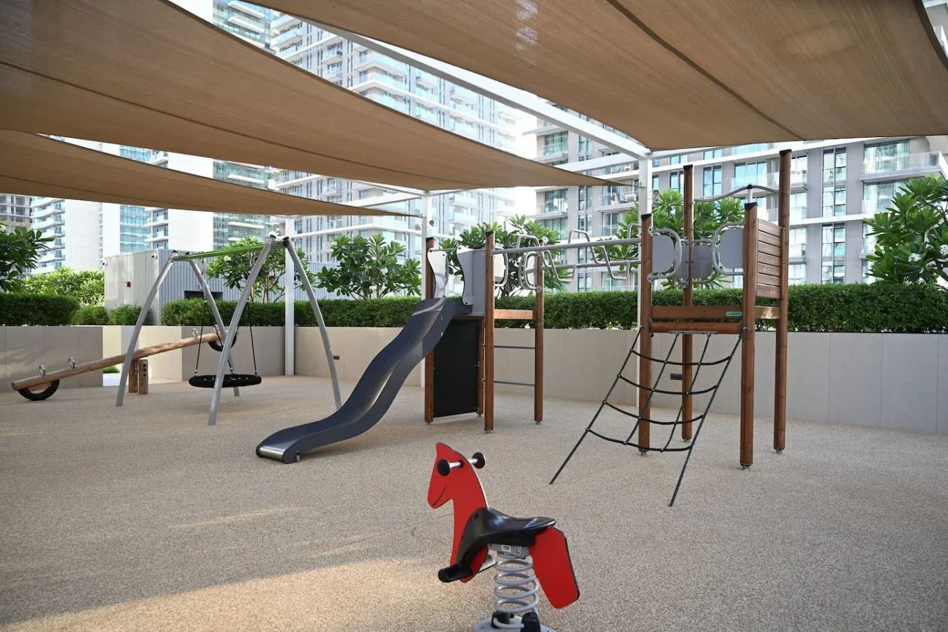 Un parque infantil exterior a la sombra, con tobogán, estructura para trepar y balancín.