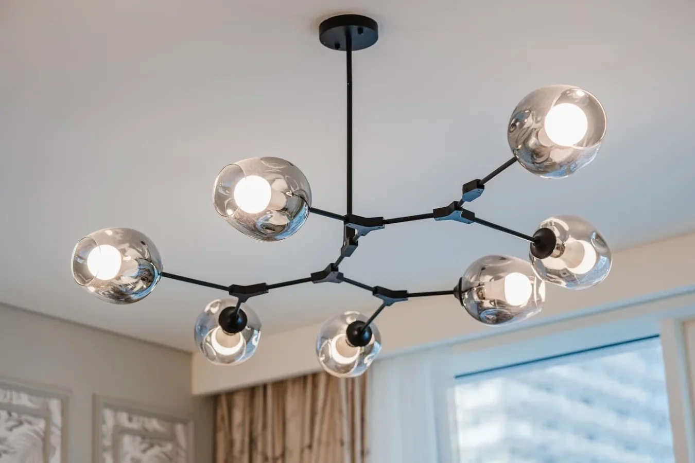Una lámpara de techo moderna con varias bombillas encendidas cuelga en una habitación luminosa.