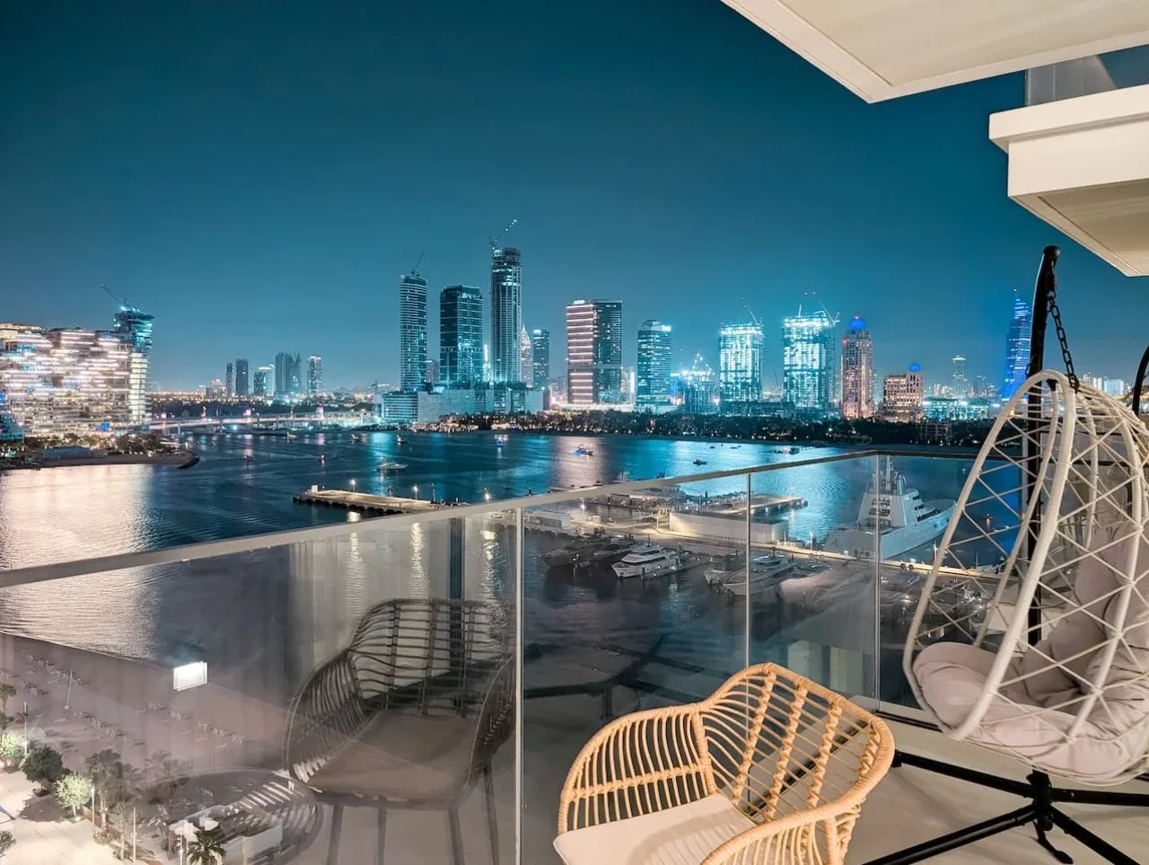 Una zona de estar en el balcón da a un horizonte urbano junto al agua por la noche.