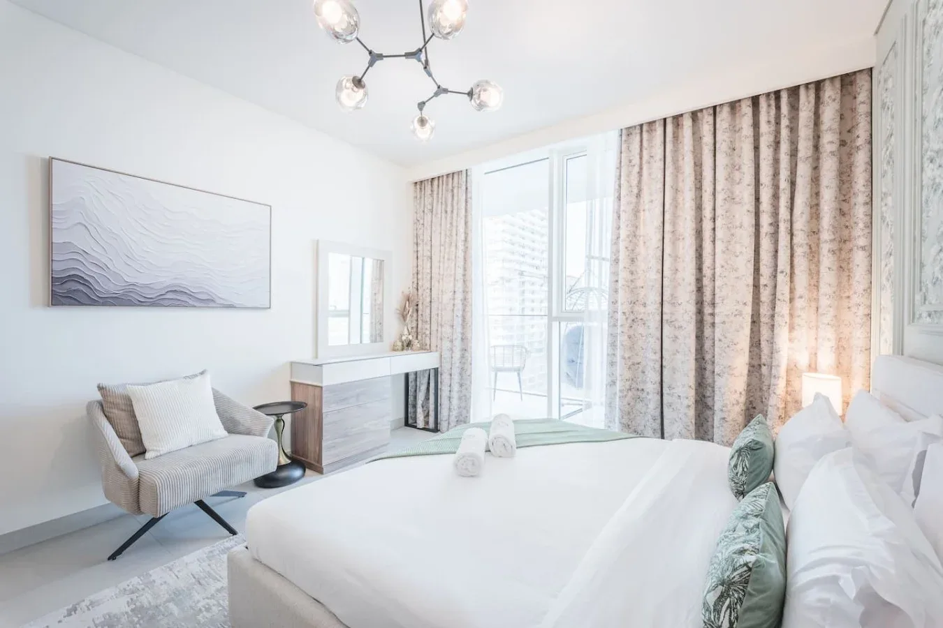Un dormitorio luminoso con una cama tendida, asientos y cortinas largas.