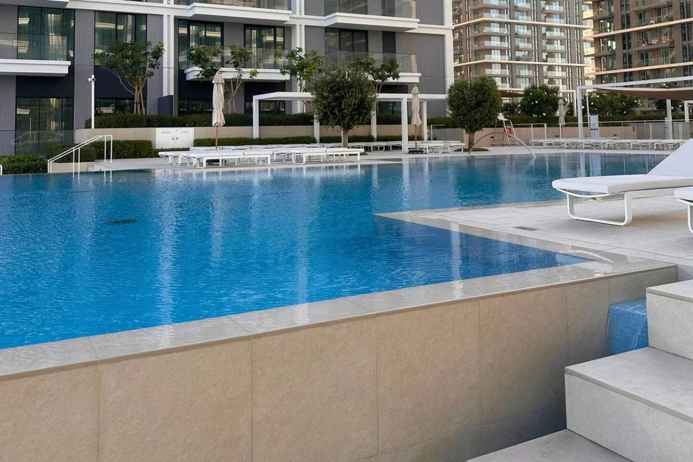 Una piscina al aire libre junto a edificios modernos y asientos junto a la piscina.