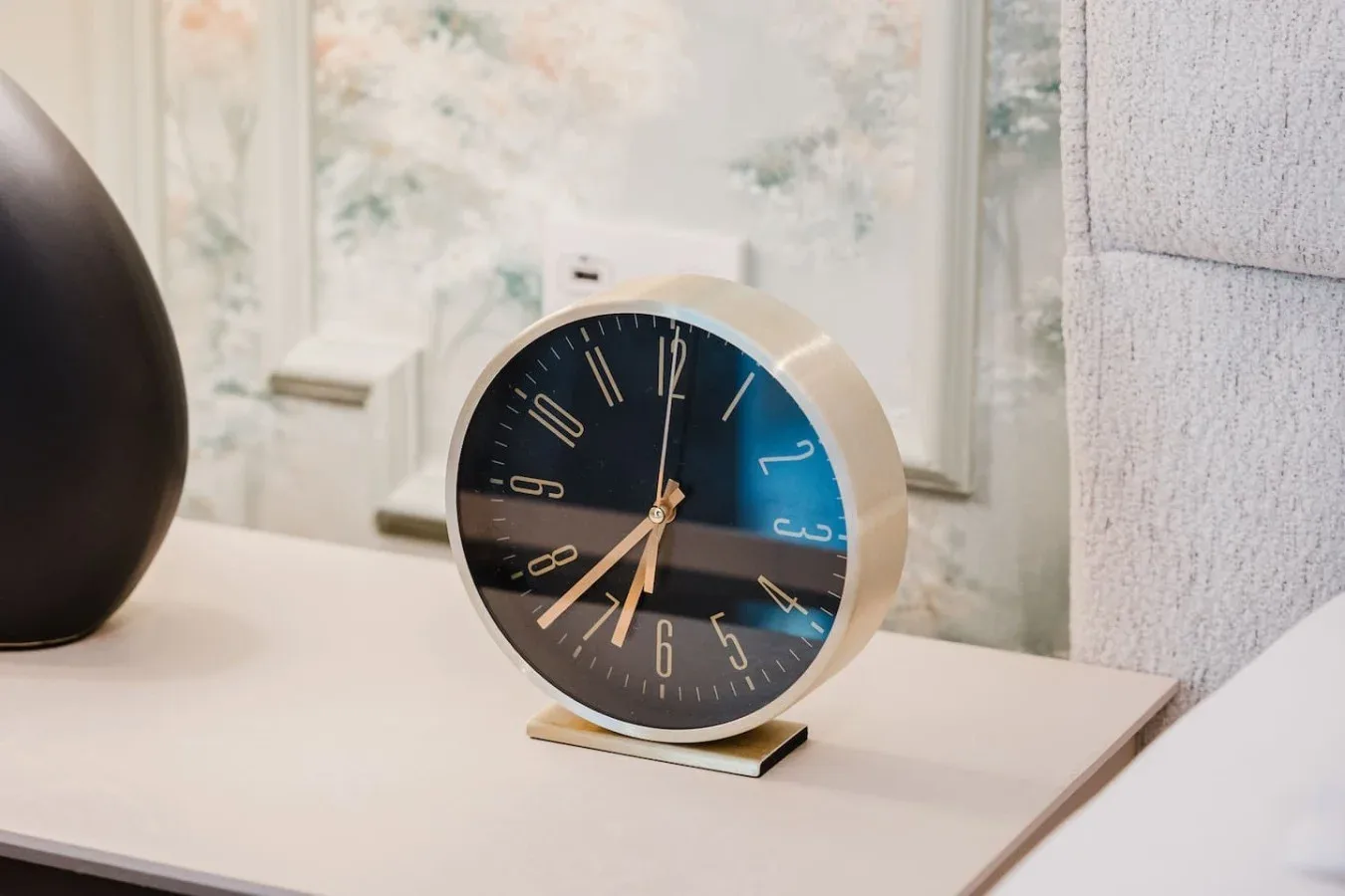 Un reloj decorativo está sobre una mesa en una habitación de tonos suaves.