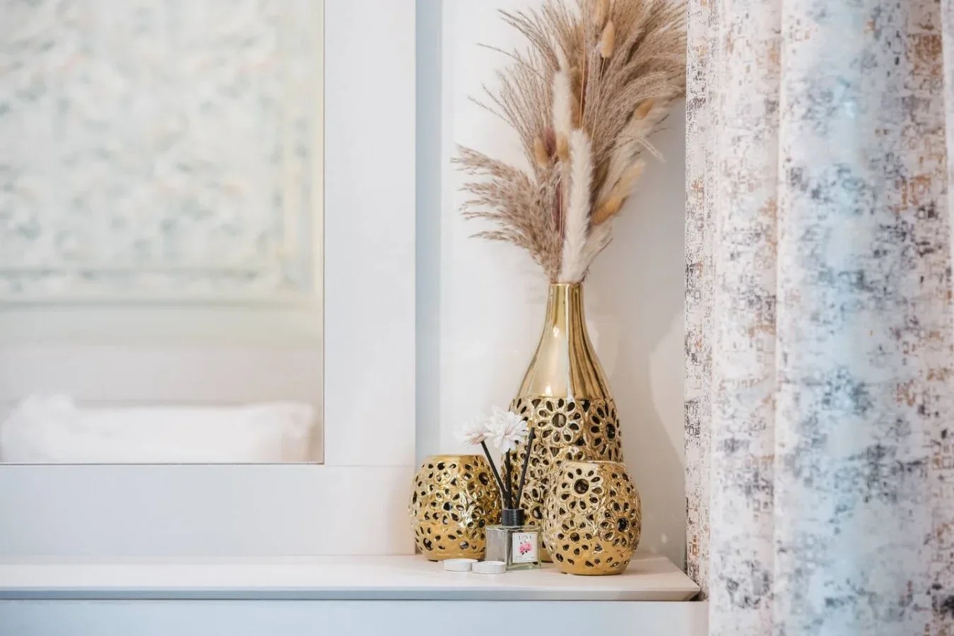 Un alféizar exhibe jarrones decorativos con hierbas secas junto a una cortina estampada.