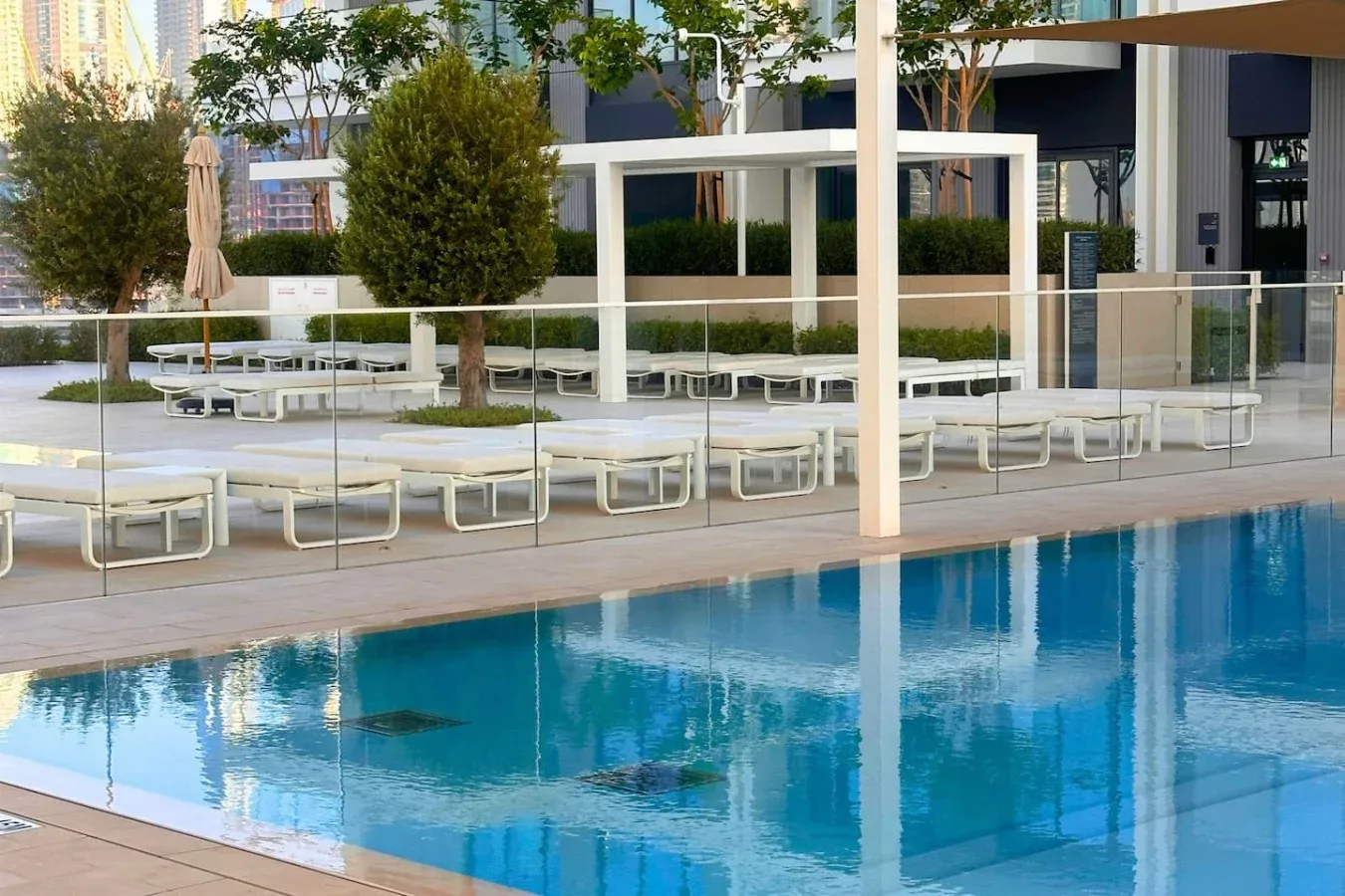 Una piscina al aire libre con asientos de descanso y una barandilla de vidrio.