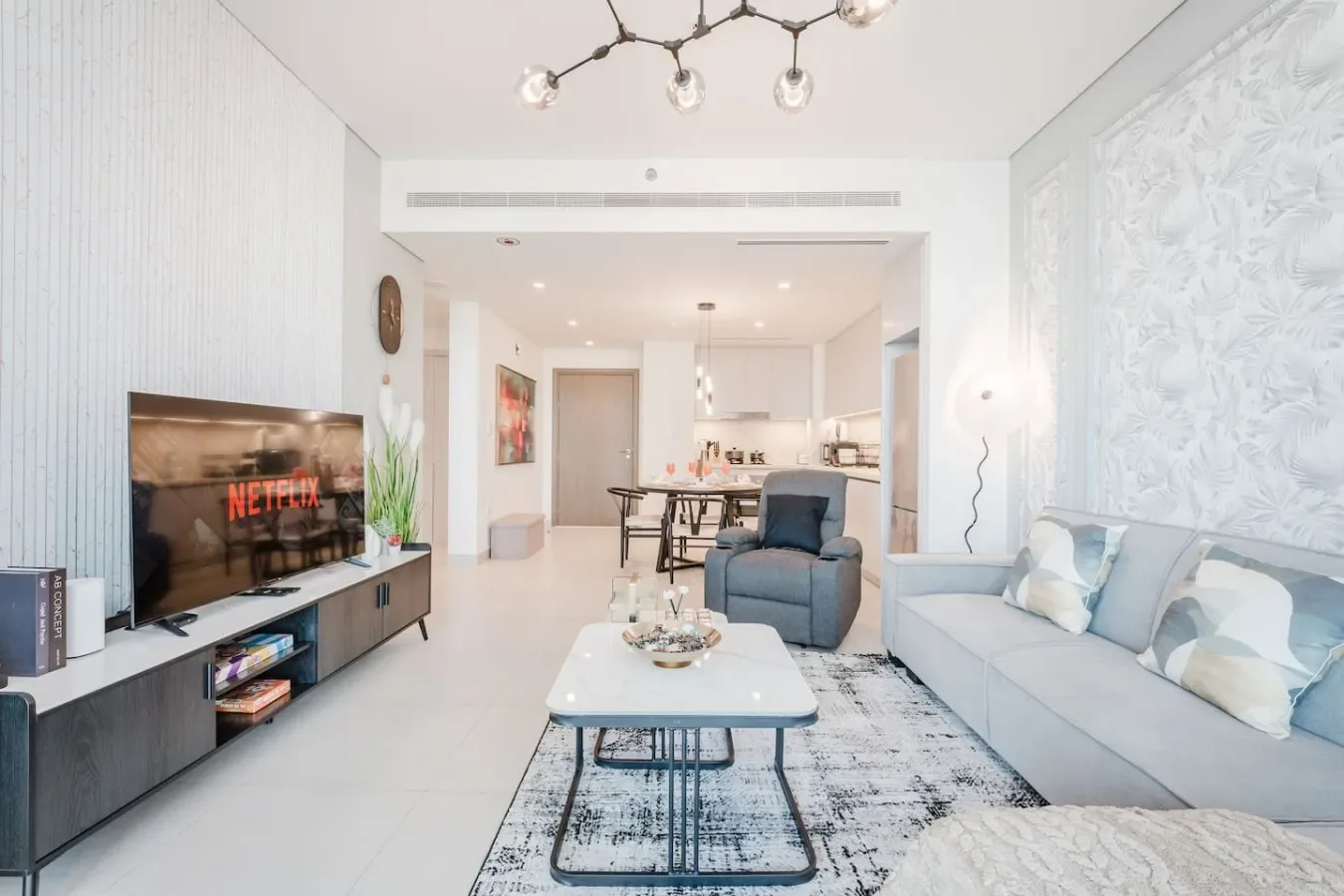 Una sala luminosa con sofá, sillón y comedor al fondo.