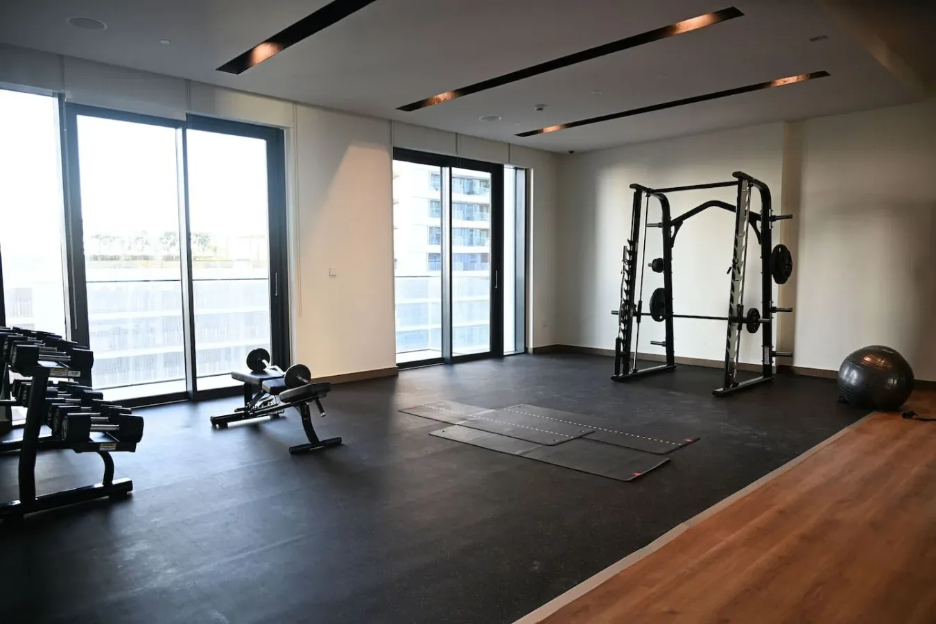 Un gimnasio con equipo de ejercicio, grandes ventanas y un suelo oscuro.