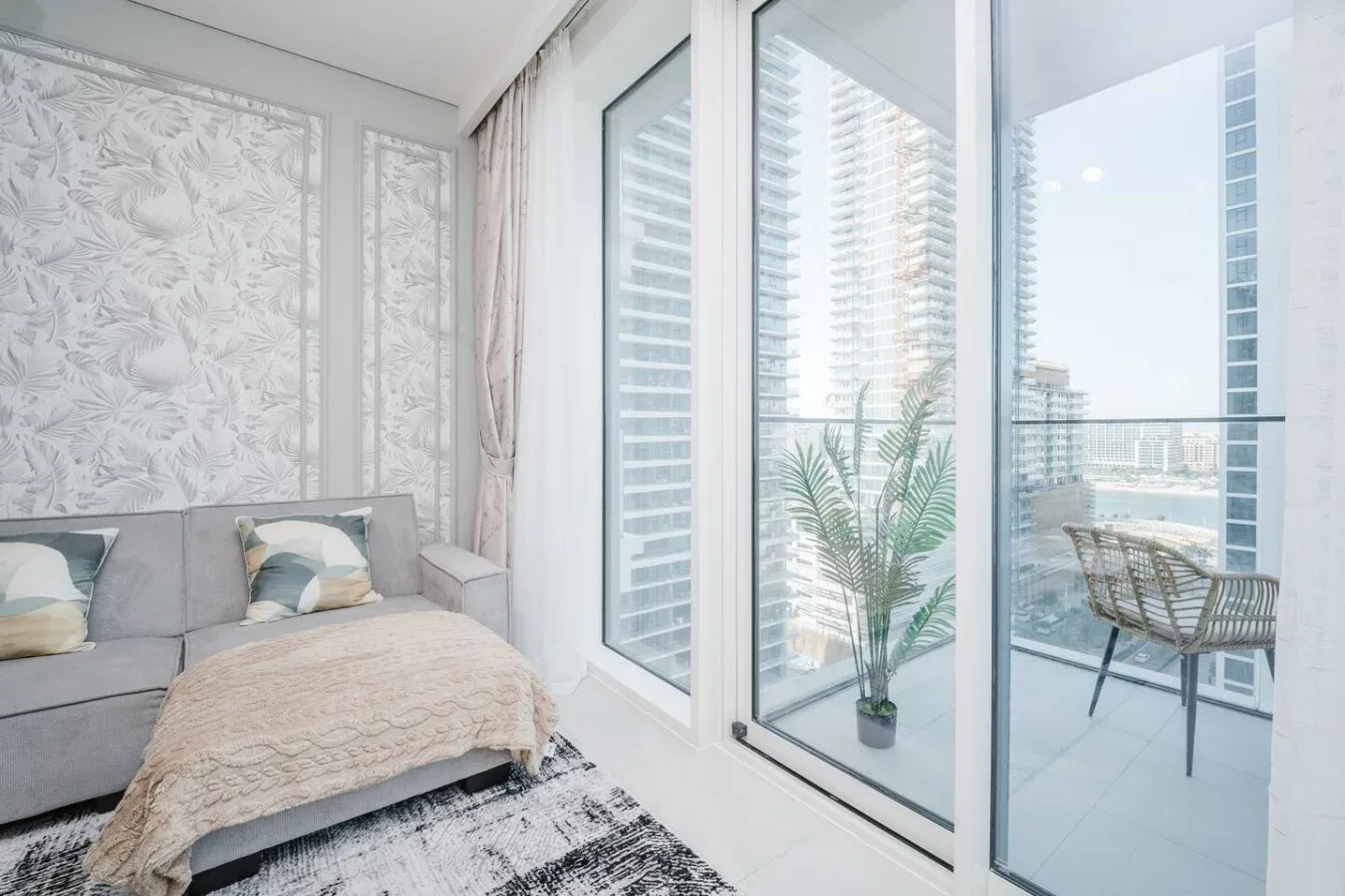 Una sala luminosa con un sofá gris junto a ventanas de piso a techo.
