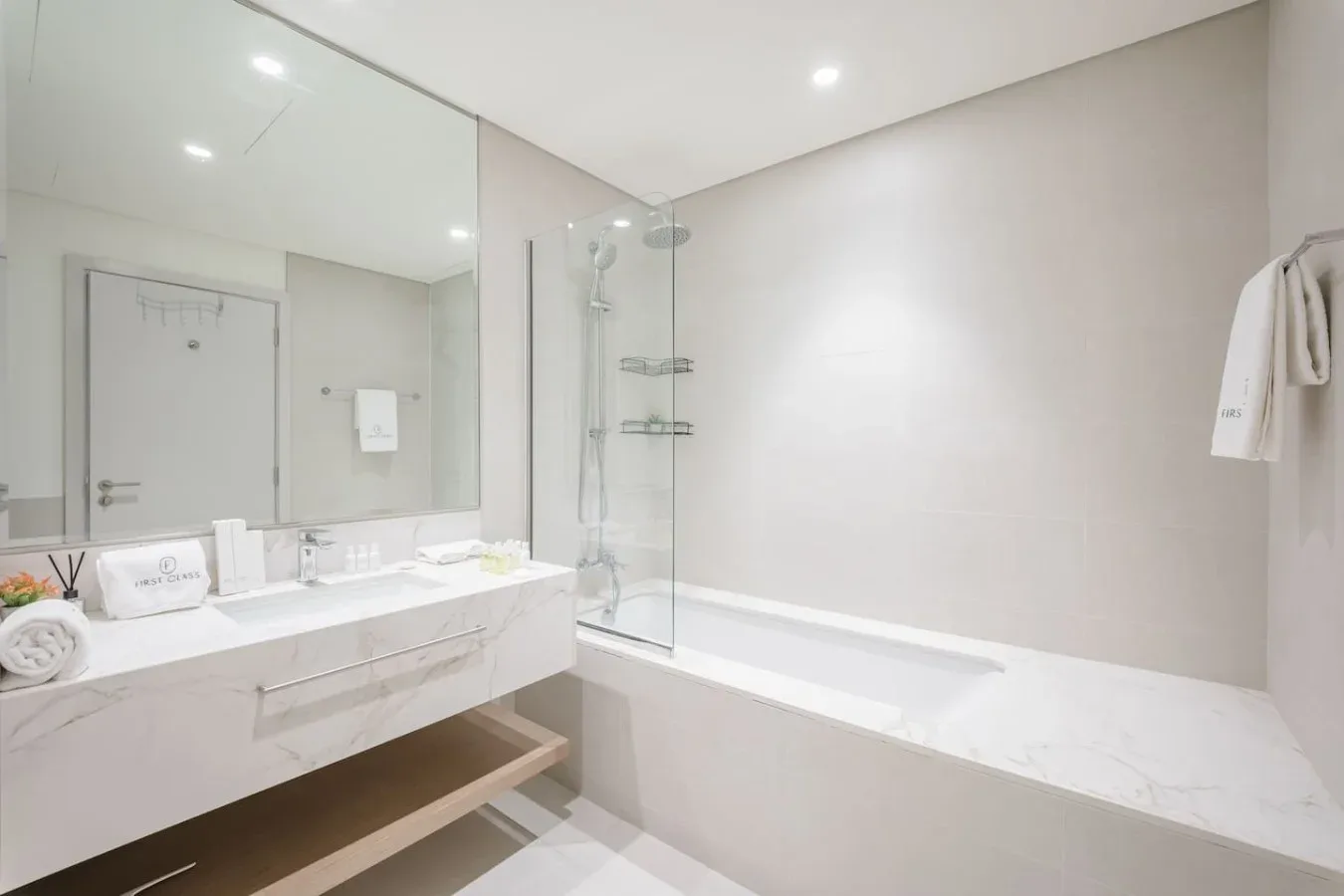 Un baño luminoso tiene una bañera junto a un lavabo con un espejo grande.
