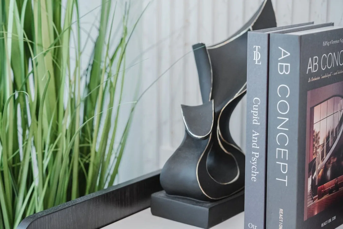 Una escultura decorativa y libros de diseño están junto a una planta frondosa.