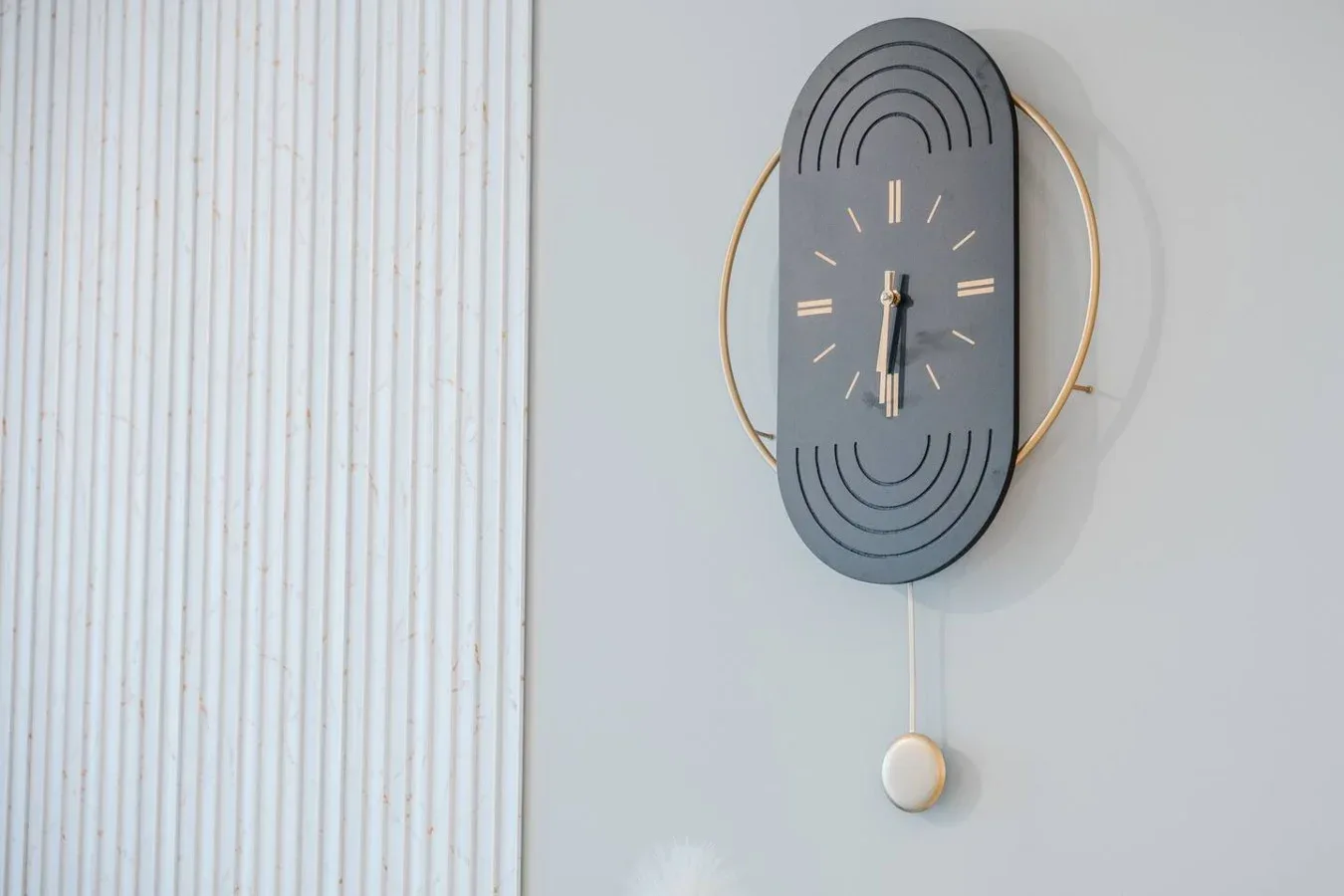 Un reloj de pared moderno cuelga junto a una pared blanca de paneles verticales.