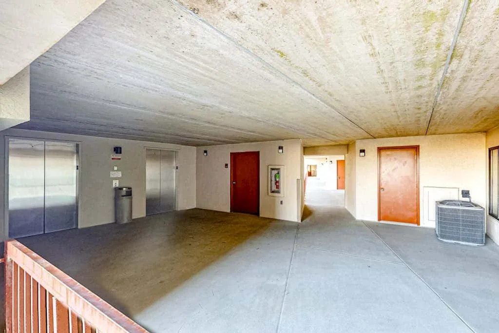 A covered concrete corridor with several doors and an air-conditioning unit.