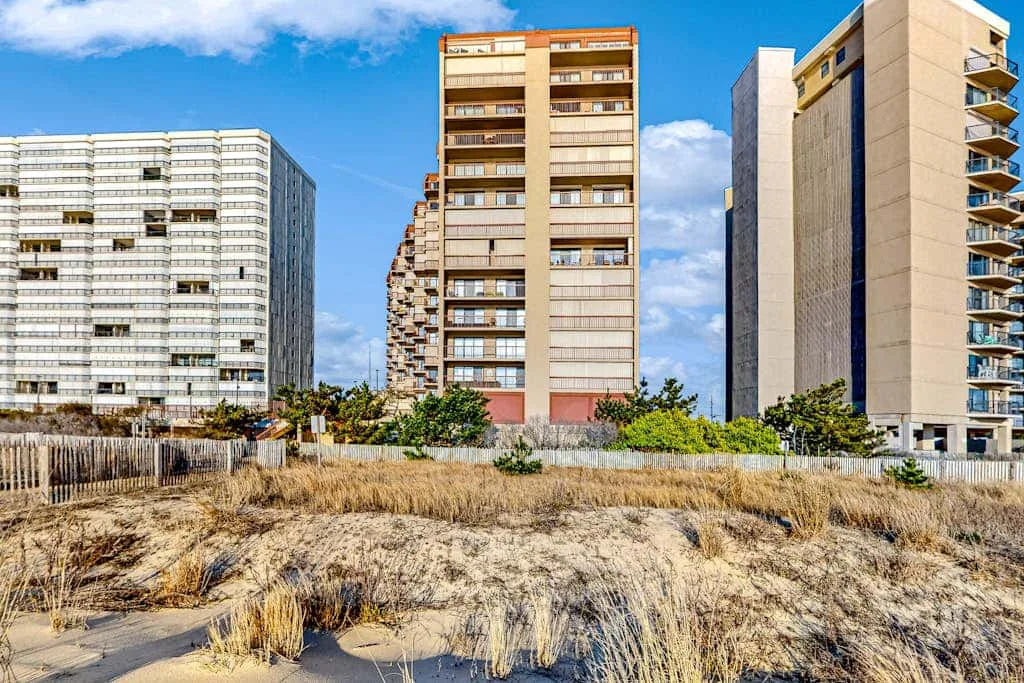 Several high-rise apartment buildings stand behind a sandy, grassy foreground.