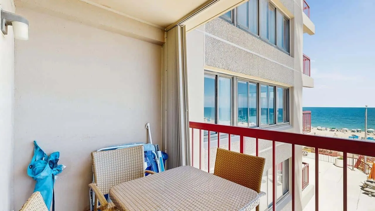 A balcony seating area with a table overlooks the beach and sea.