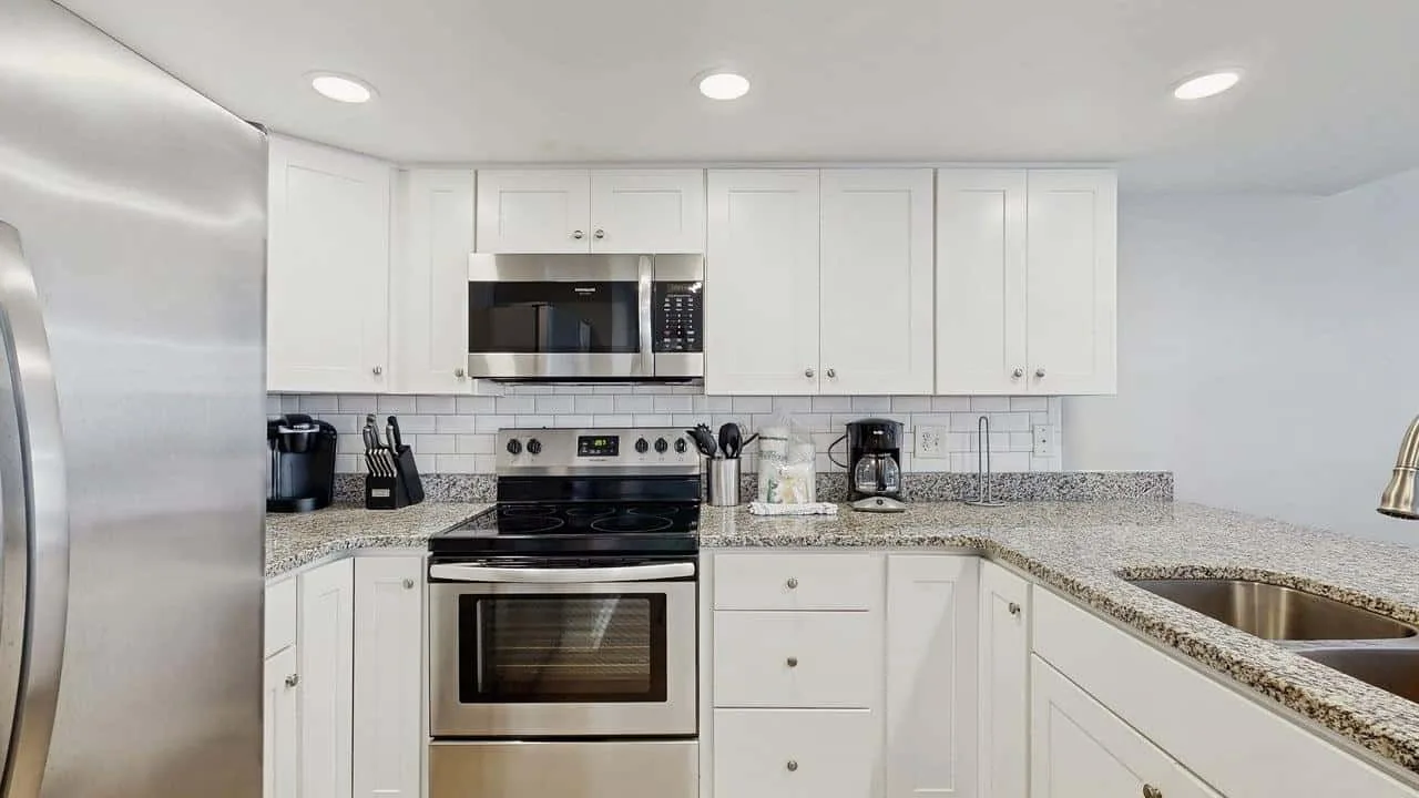A bright kitchen with white cabinets, stainless steel appliances, and stone countertops.