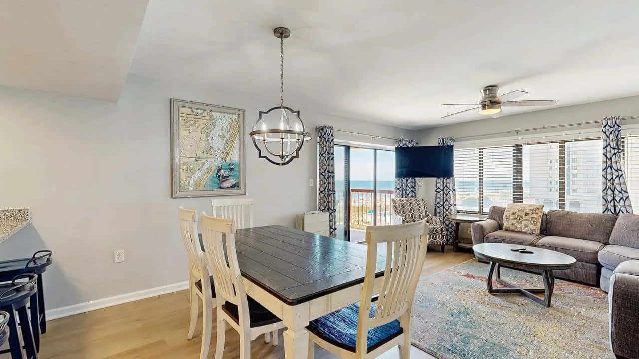 A dining table and seating sit beside a bright living room with wide windows.