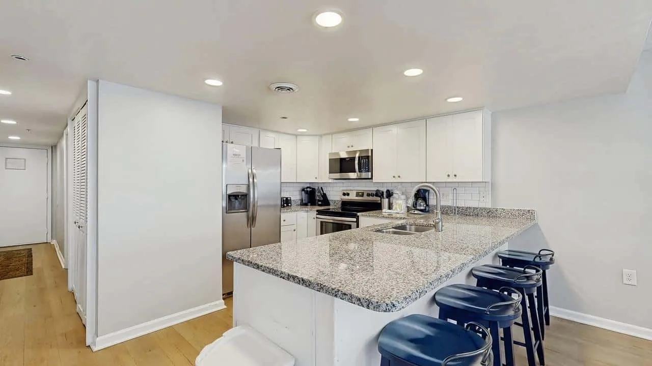 A bright kitchen with white cabinetry, stainless steel appliances, and a large granite island.
