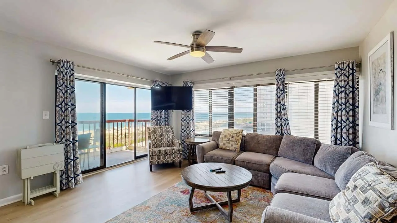 A bright living room with a sectional sofa, coffee table, and windows overlooking the water.