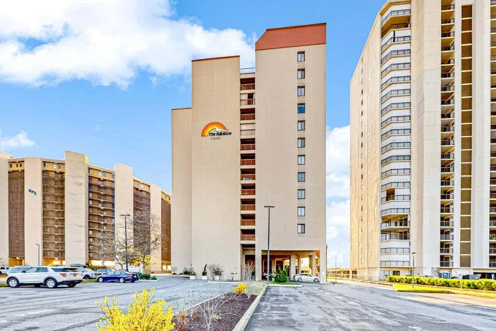 Apartment buildings surround a paved parking area beneath a partly cloudy sky.