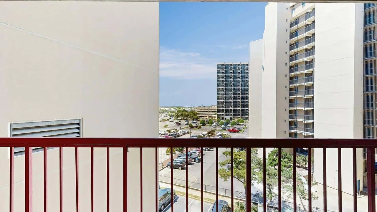 An outdoor balcony overlooks nearby buildings, a street, and parking.