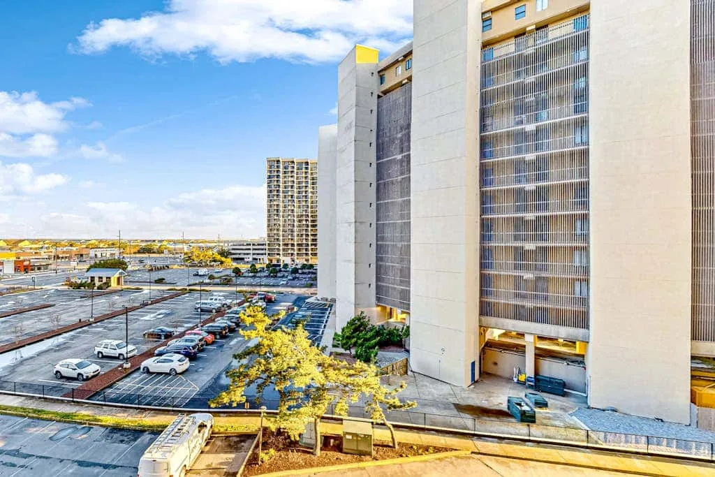 A tall office building overlooks a parking lot beneath a partly cloudy sky.