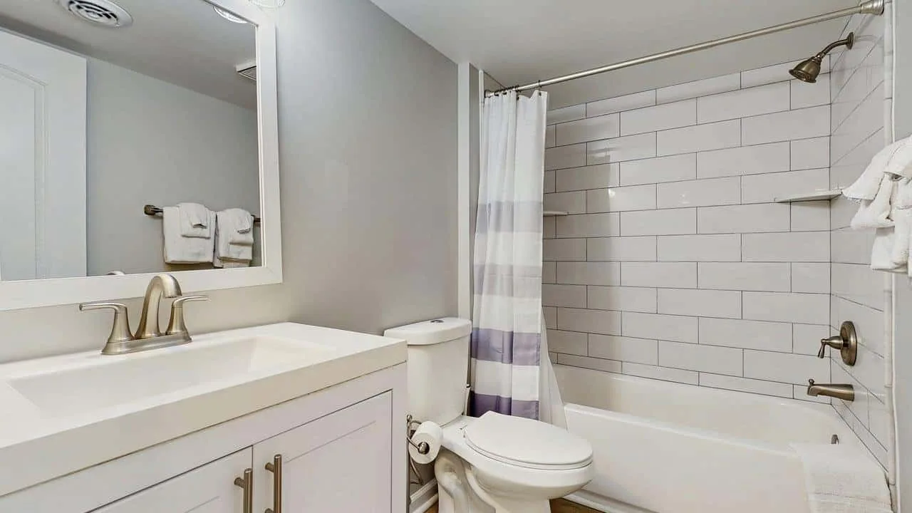 A bathroom with a bathtub, shower curtain, toilet, and vanity.