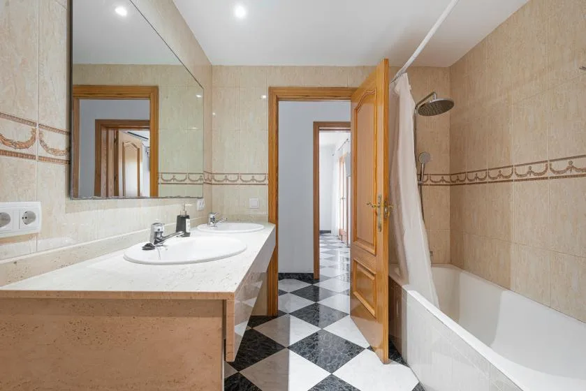 Un baño con lavabo, espejo y bañera junto a una puerta de madera abierta.