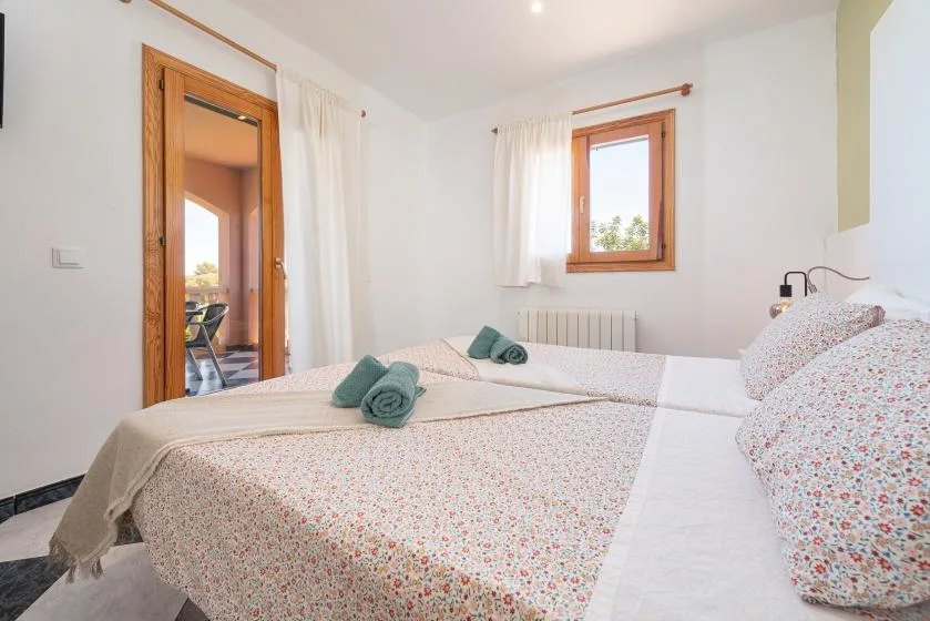 Un dormitorio luminoso con ropa de cama floral y una ventana con cortinas transparentes.