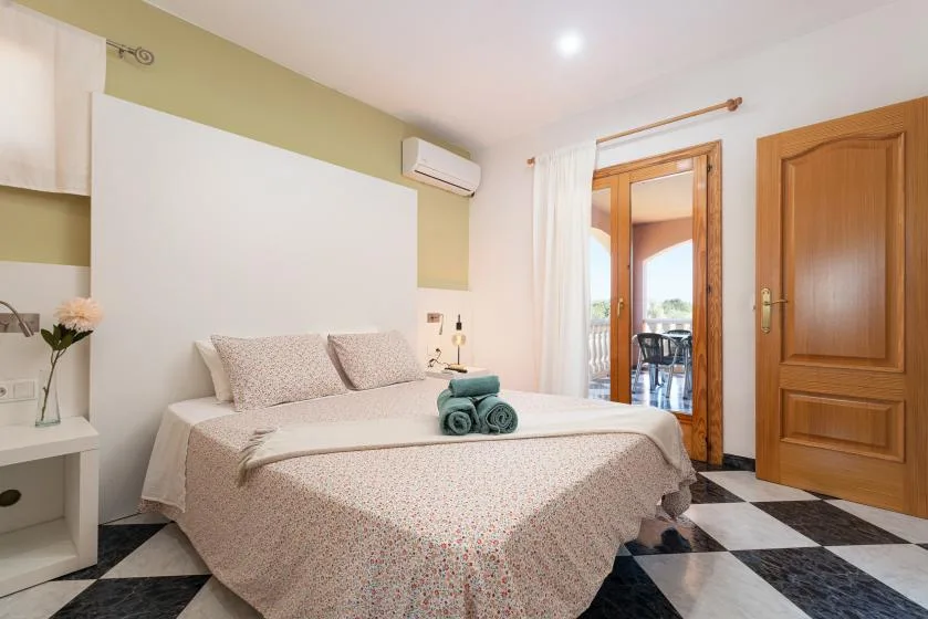Un dormitorio con una cama bien hecha y una puerta de madera abierta a un balcón.