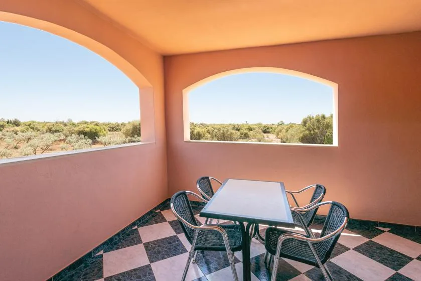 Un patio cubierto con mesa y asientos junto a aberturas arqueadas con vistas a la vegetación.