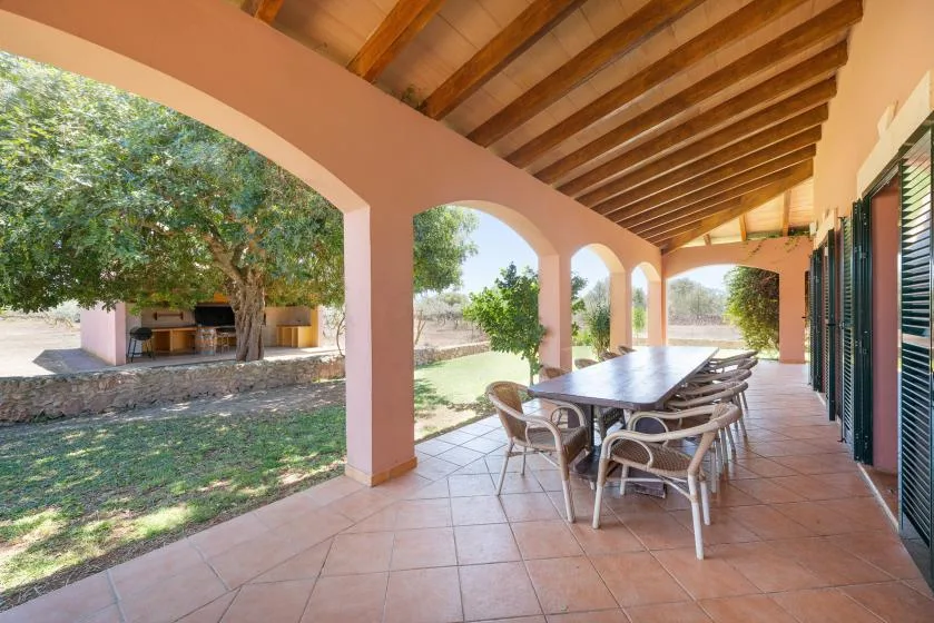 Un patio cubierto con una mesa de comedor da a un jardín a través de arcos abiertos.