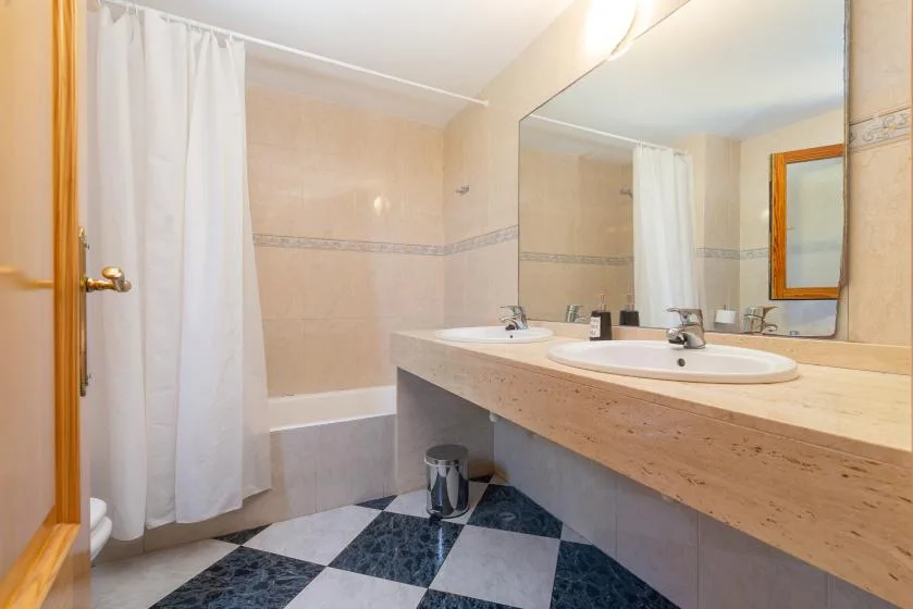 Un baño con lavabo doble, espejo grande y cortina de ducha.