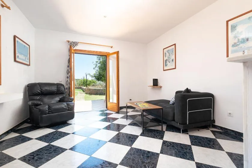 Una sala luminosa con asientos, una mesa de centro y una puerta abierta al jardín.