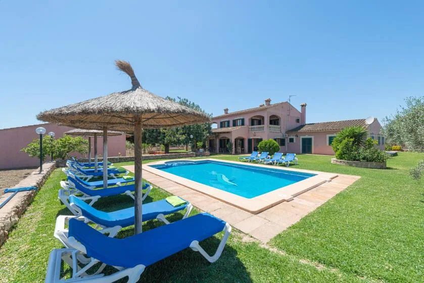 Una piscina al aire libre está junto a un césped y un edificio rosa.