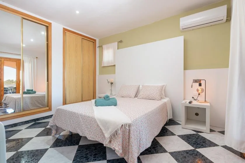 Un dormitorio con una cama, un armario con espejo y suelo de baldosas blancas y negras.