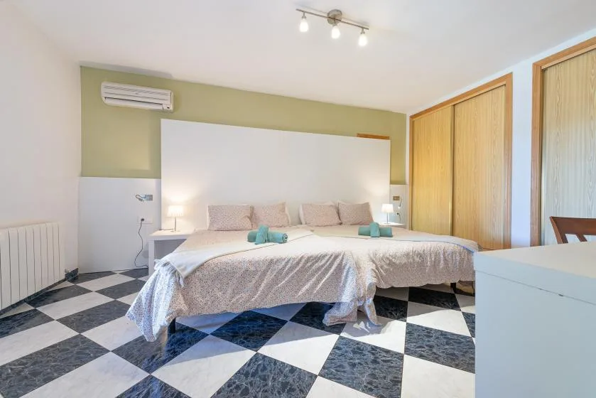Un dormitorio con una cama, mesitas de noche y suelo de baldosas a cuadros.