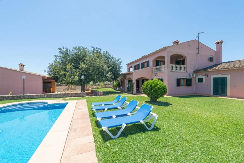 Una casa rosa da a una piscina y un césped con tumbonas azules.