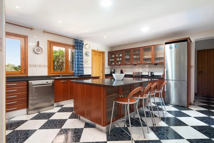 Una cocina con armarios de madera, una isla central y un suelo de baldosas blancas y negras.