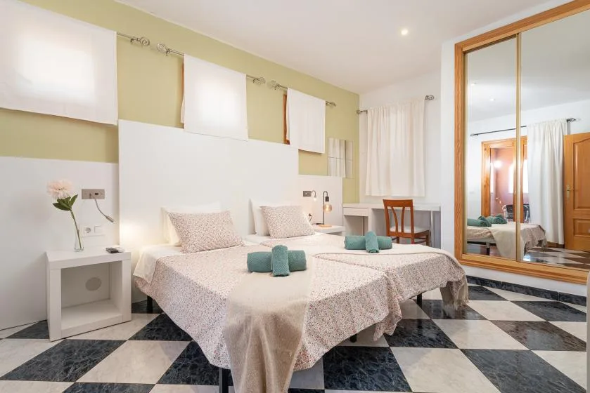 Un dormitorio con dos camas, una mesa pequeña y un gran espejo de pared.