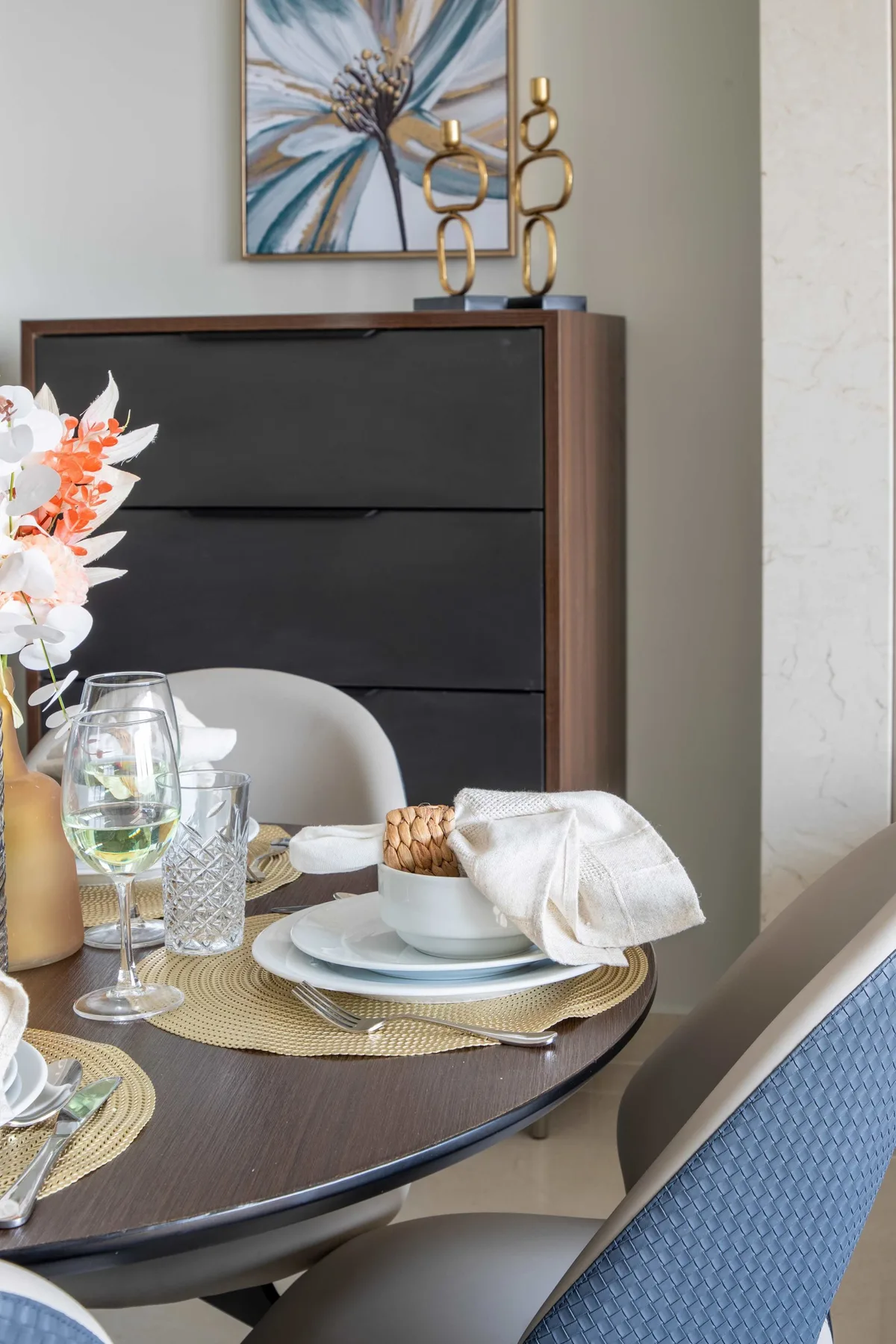 A dining table is set with plates, glasses, and a folded napkin beside a dark cabinet.