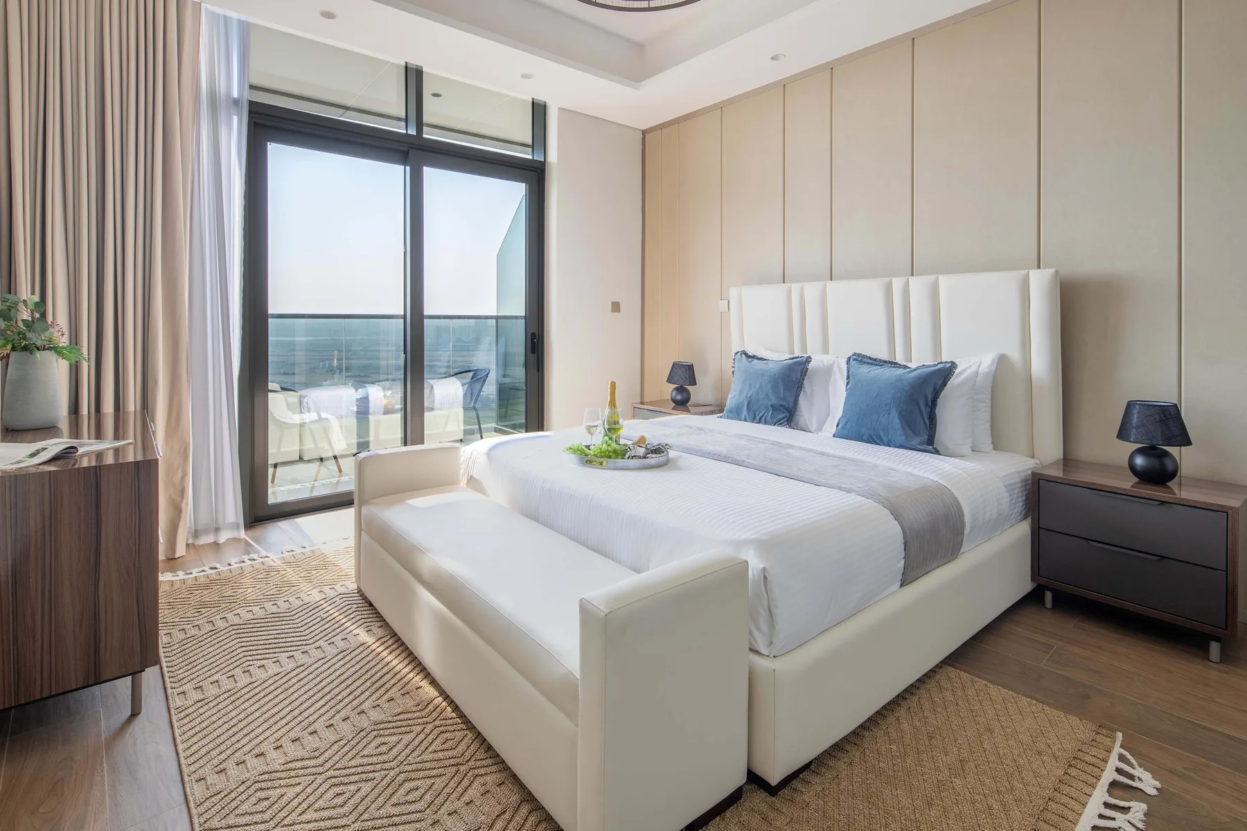 A bright bedroom with a bed beside large windows overlooking the water.