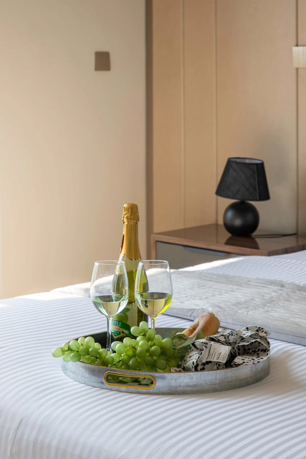 A bedroom with a tray of grapes, wine glasses, and a bottle on the bed.